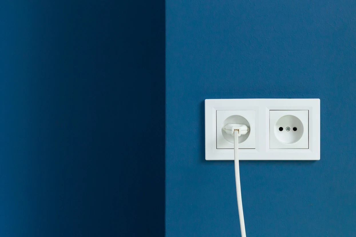 Mur intérieur bleu avec double prise électrique murale blanche, une prise occupée par un câble d'alimentation blanc branché