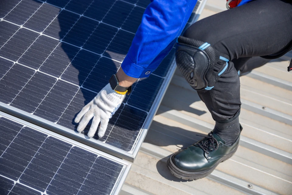 Ouvrier en équipement de protection individuelle avec casque jaune et harnais de sécurité travaillant sur installation de panneaux solaires photovoltaïques